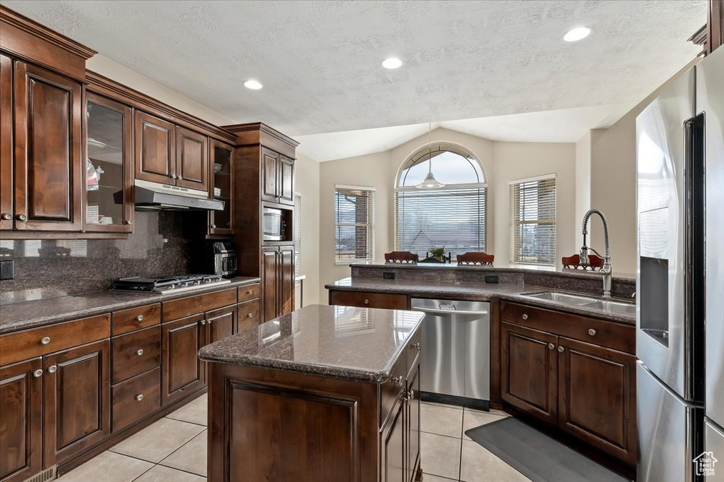Kitchen featuring light tile floors, tasteful backsplash, vaulted ceiling, a center island, and stainless steel appliances