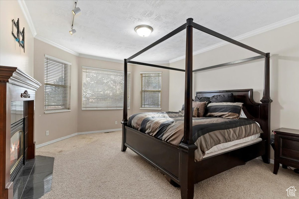 Bedroom with light carpet, a textured ceiling, ornamental molding, a tiled fireplace, and rail lighting
