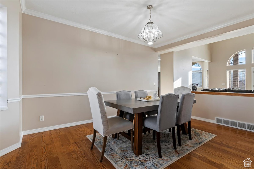 Dining space with dark wood-type flooring, a notable chandelier, and ornamental molding