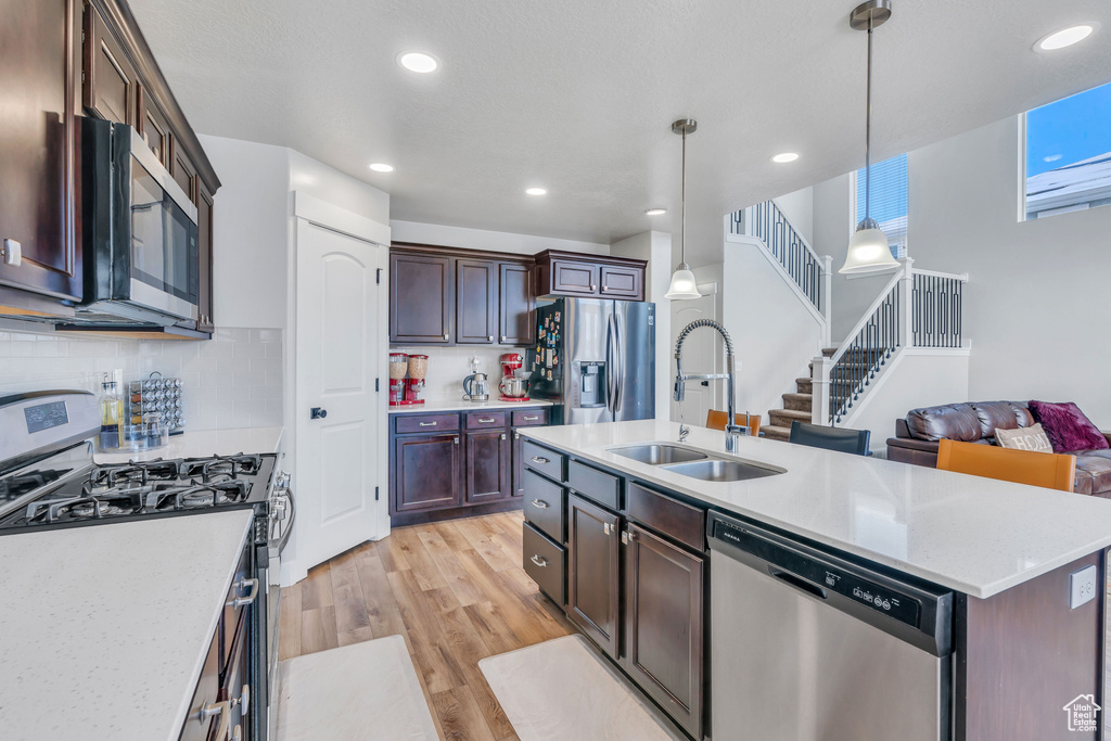 Kitchen with decorative light fixtures, appliances with stainless steel finishes, light hardwood / wood-style flooring, sink, and tasteful backsplash