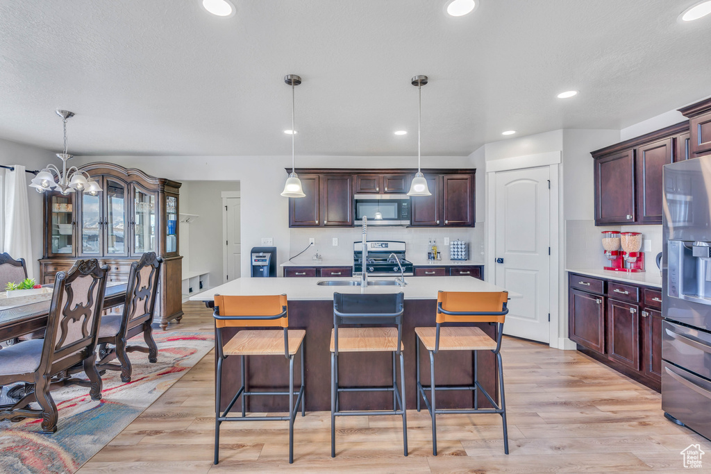 Kitchen with hanging light fixtures, appliances with stainless steel finishes, a kitchen island with sink, and light hardwood / wood-style flooring