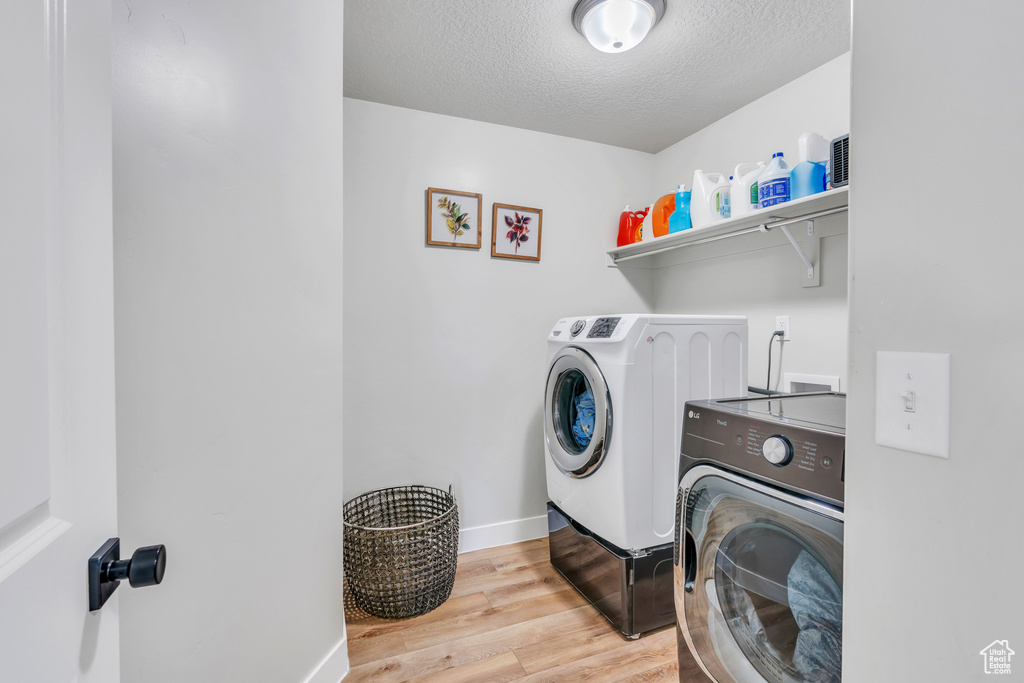 Clothes washing area featuring light wood-type flooring, hookup for a washing machine, a textured ceiling, and washer and dryer