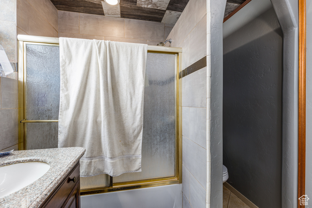 Full bathroom with tile walls, shower / bath combination with glass door, toilet, and vanity