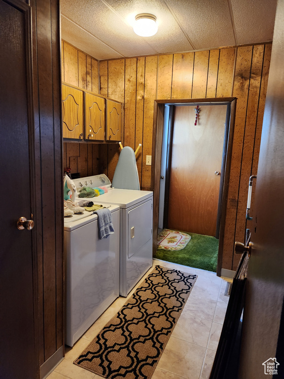 Clothes washing area with wood walls, cabinets, washing machine and clothes dryer, and light tile floors