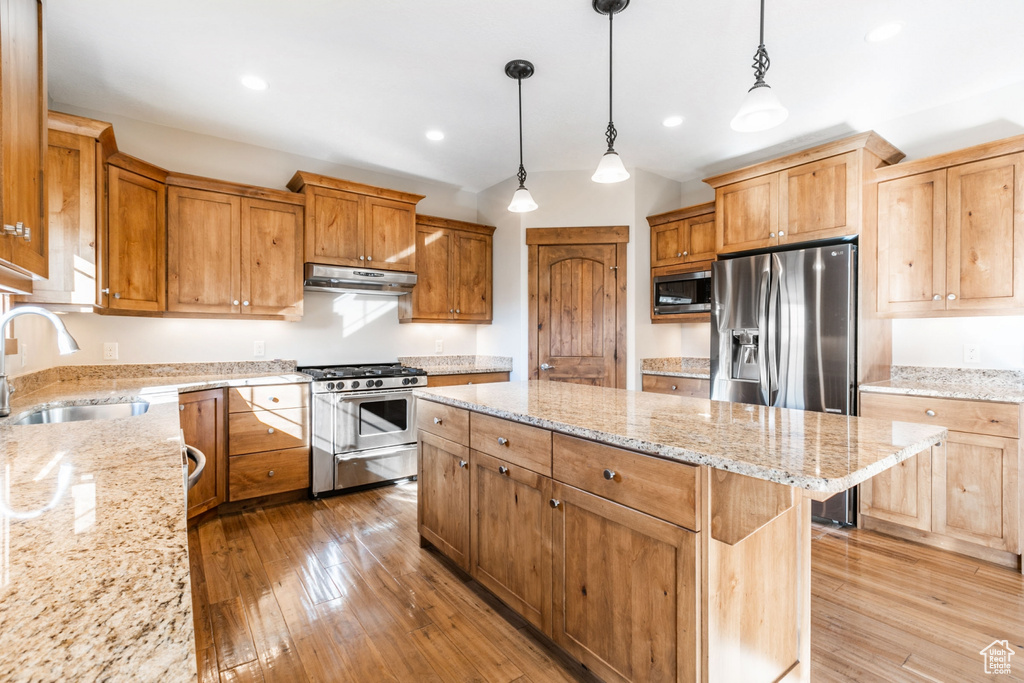 Kitchen featuring decorative light fixtures, stainless steel appliances, light stone counters, sink, and hardwood / wood-style floors