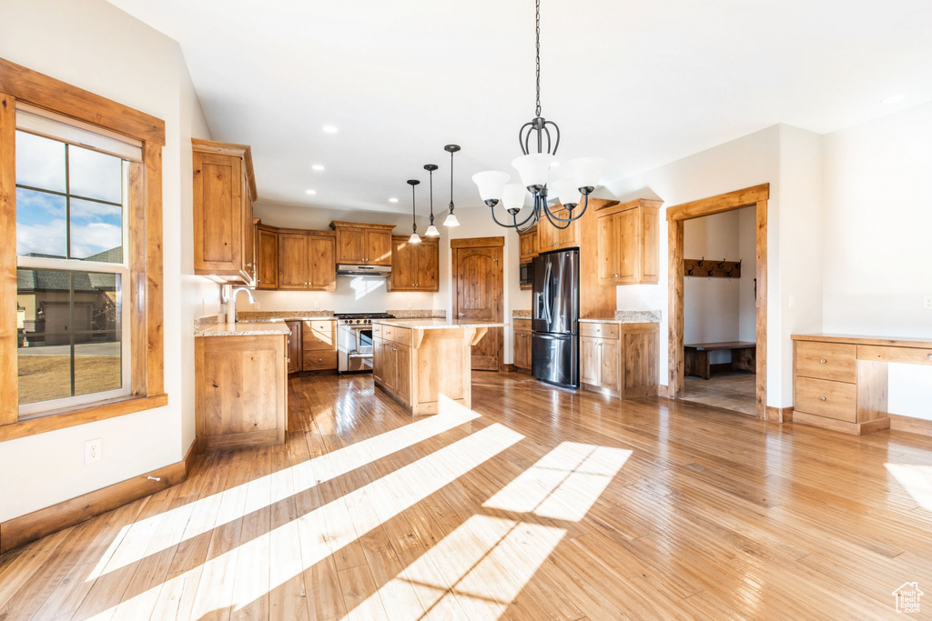 Kitchen featuring decorative light fixtures, light hardwood / wood-style floors, appliances with stainless steel finishes, a notable chandelier, and a kitchen island