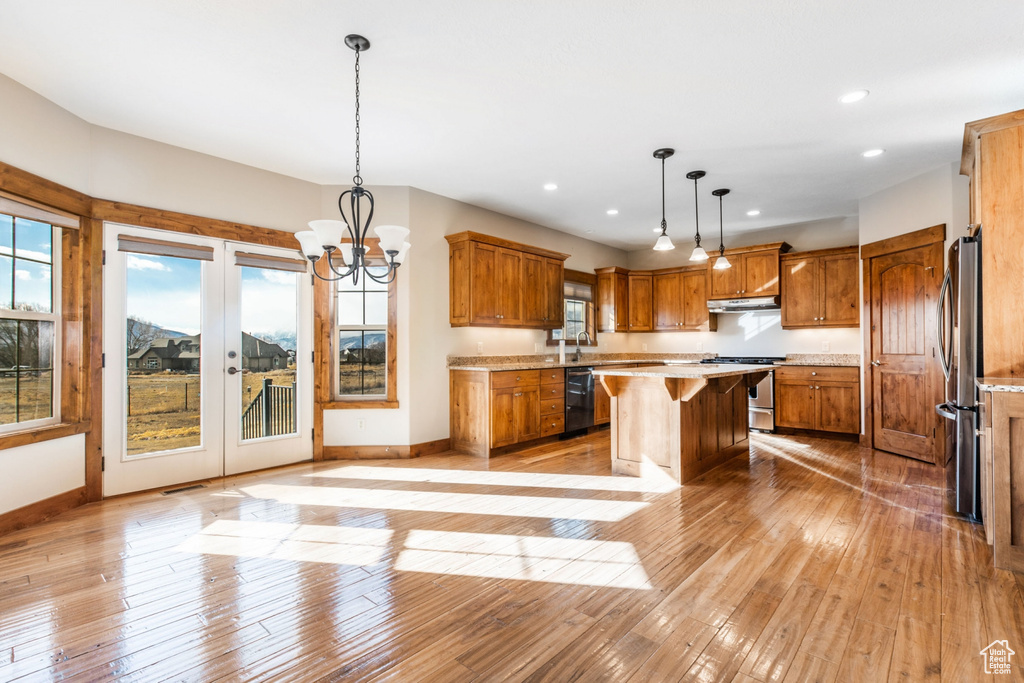 Kitchen with an inviting chandelier, pendant lighting, stainless steel appliances, hardwood / wood-style flooring, and a kitchen island