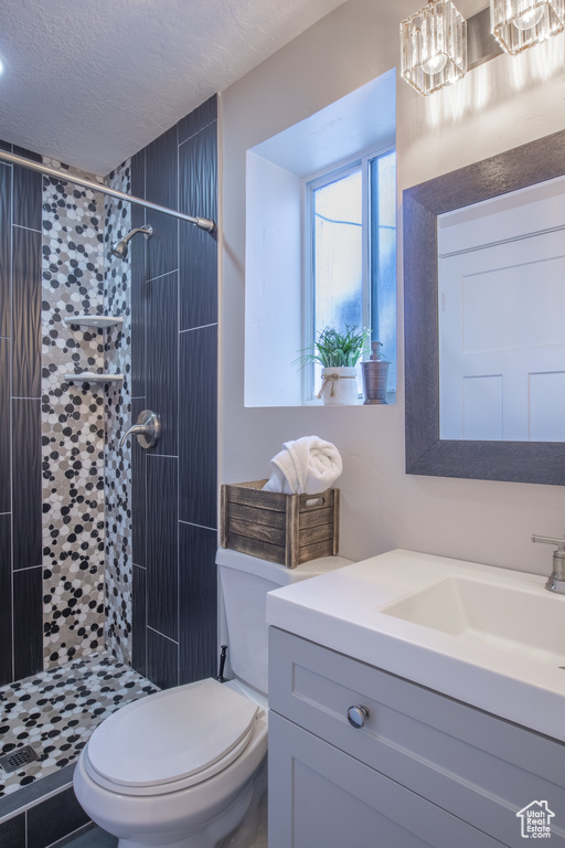 Bathroom with tiled shower, toilet, a textured ceiling, and oversized vanity