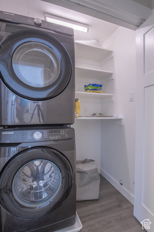 Laundry room featuring dark wood-type flooring and stacked washer / dryer