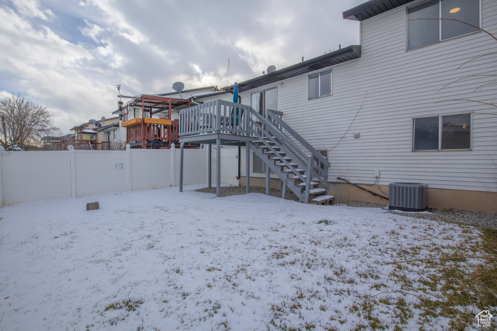 Snow covered rear of property featuring central AC unit and a wooden deck