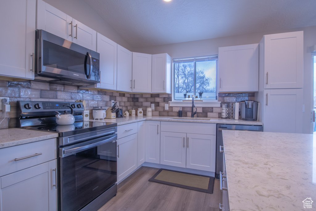 Kitchen featuring white cabinets, light hardwood / wood-style floors, stainless steel appliances, sink, and tasteful backsplash