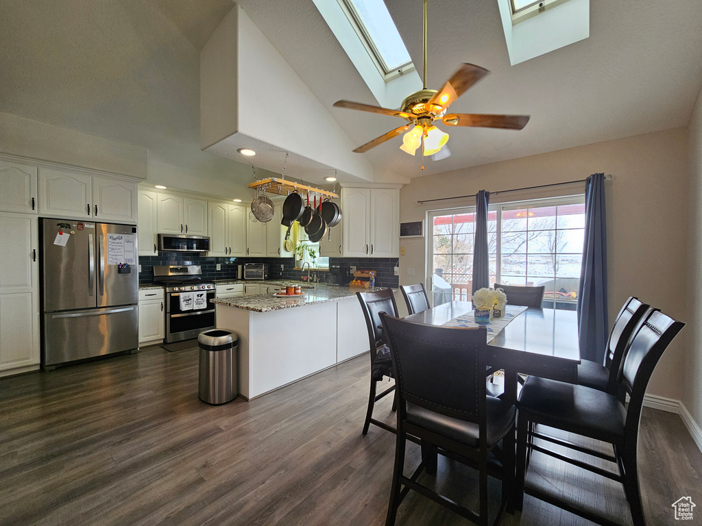 Dining room with ceiling fan, dark wood-type flooring, a skylight, high vaulted ceiling, and sink