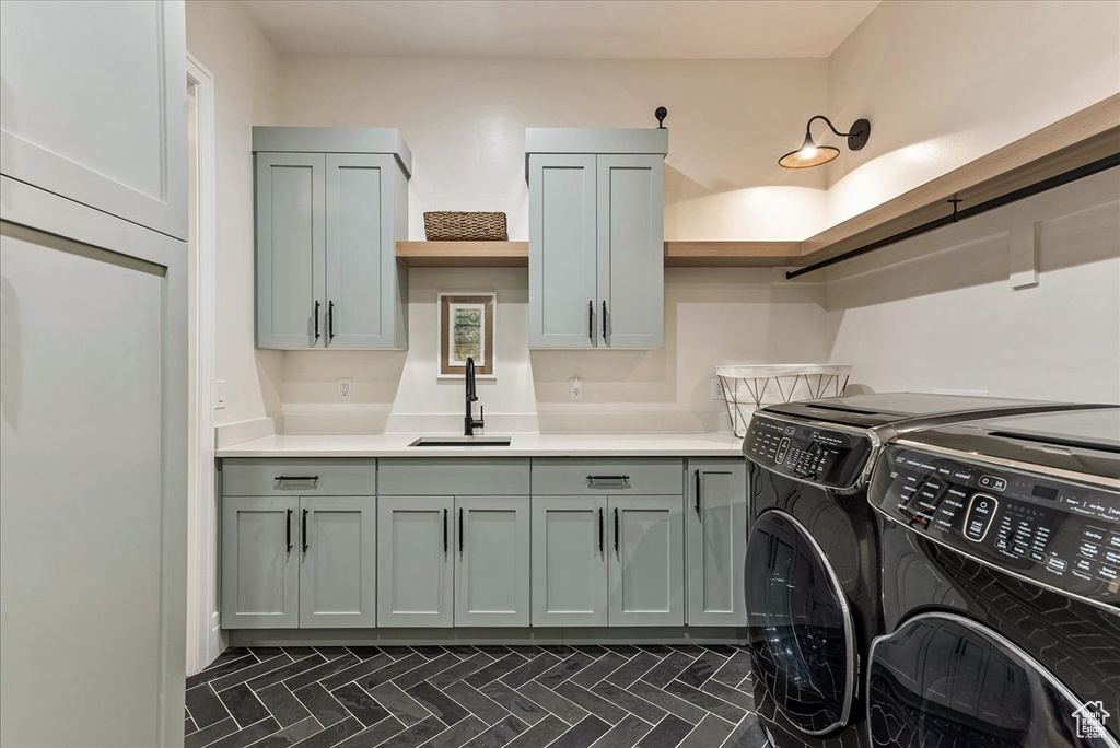 Washroom with dark tile flooring, independent washer and dryer, cabinets, and sink