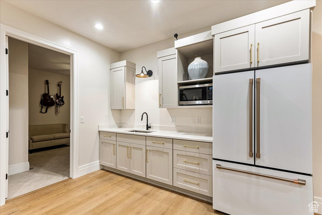 Kitchen with high end fridge, light hardwood / wood-style flooring, sink, stainless steel microwave, and gray cabinetry