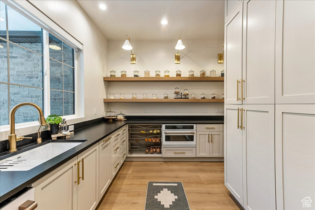 Kitchen with dishwasher, light hardwood / wood-style flooring, sink, white cabinetry, and stainless steel oven