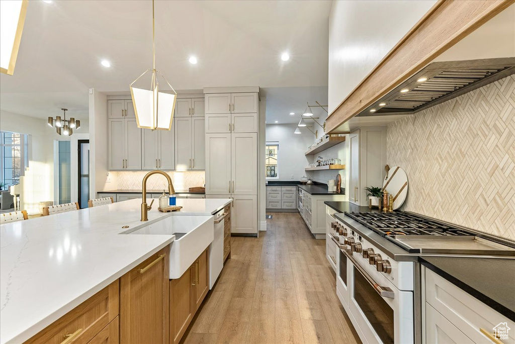 Kitchen with light hardwood / wood-style floors, tasteful backsplash, double oven range, decorative light fixtures, and white cabinets