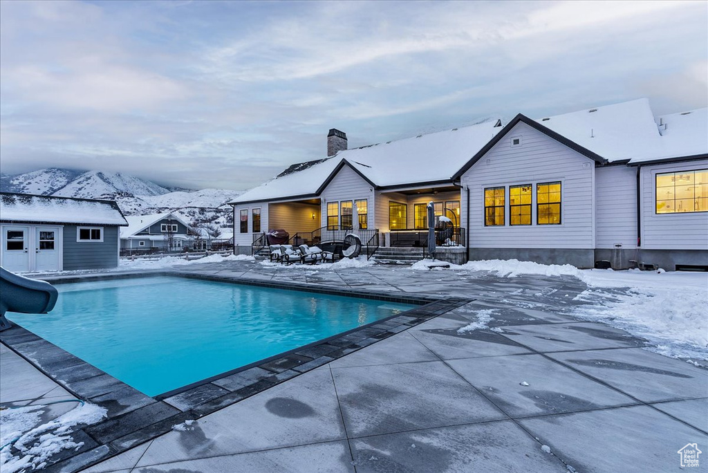 Snow covered pool with a water slide, a patio, and a mountain view