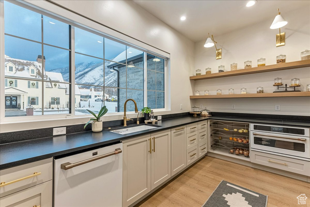 Kitchen featuring white dishwasher, light wood-type flooring, stainless steel oven, white cabinets, and sink
