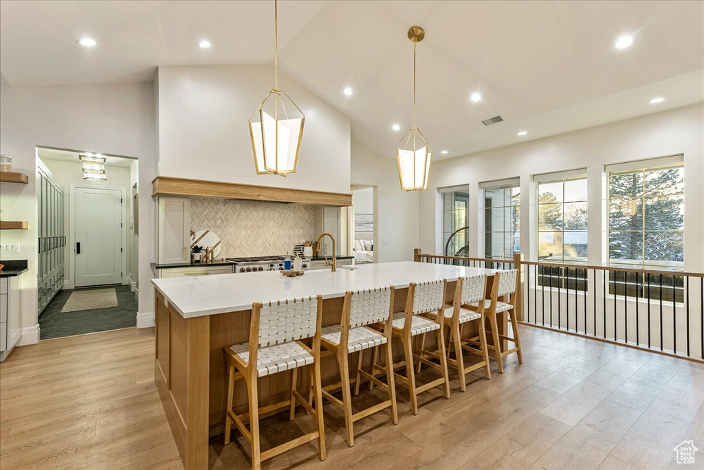 Kitchen featuring pendant lighting, a breakfast bar area, light wood-type flooring, high vaulted ceiling, and an island with sink