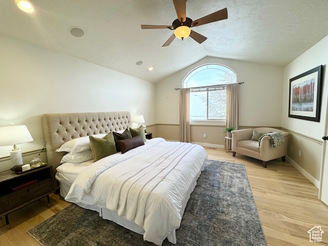 Bedroom featuring light hardwood / wood-style floors, a textured ceiling, lofted ceiling, and ceiling fan