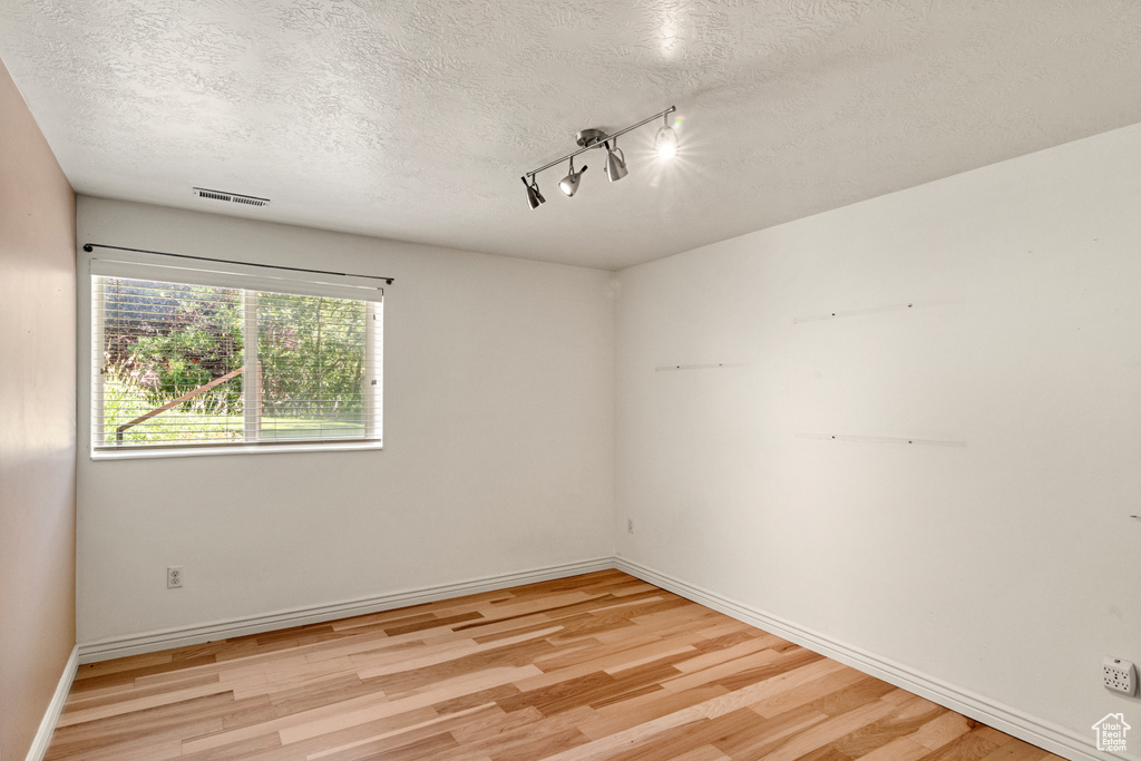 Spare room with rail lighting, a textured ceiling, and light hardwood / wood-style floors