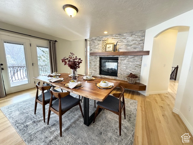 Dining area with a stone fireplace, light wood-type flooring, and a textured ceiling