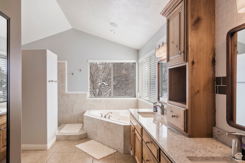 Bathroom with vaulted ceiling, a relaxing tiled bath, double sink vanity, and tile flooring