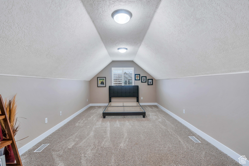 Bonus room with carpet floors, lofted ceiling, and a textured ceiling