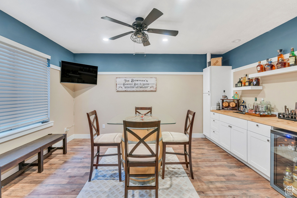 Dining area with bar area, light hardwood / wood-style floors, beverage cooler, and ceiling fan