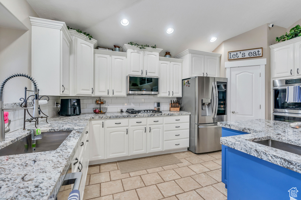Kitchen featuring stainless steel appliances, tasteful backsplash, white cabinetry, and lofted ceiling