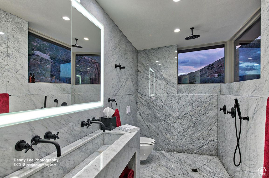 Bathroom with toilet, vanity, tile walls, tile flooring, and a tile shower