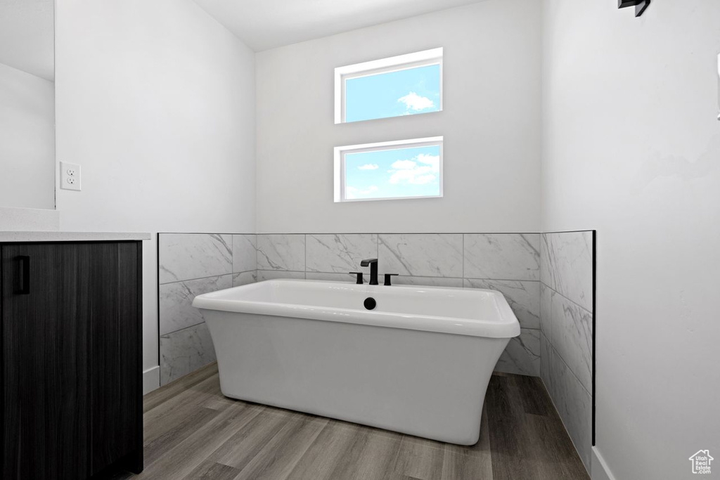 Bathroom with hardwood / wood-style floors, a bathing tub, and tile walls