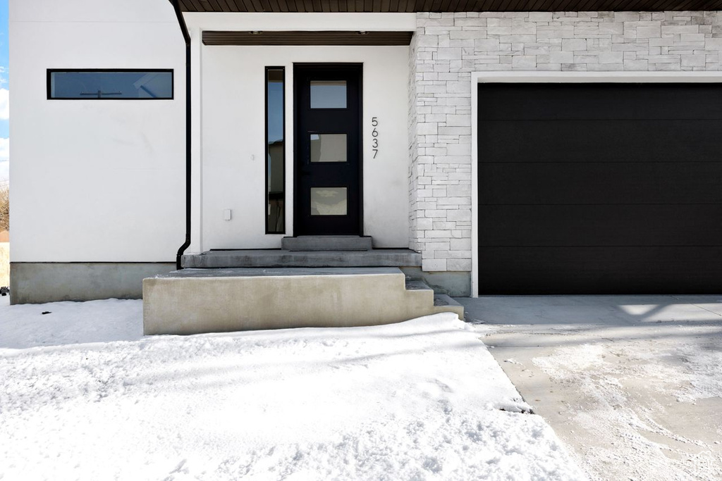 Snow covered property entrance featuring a garage