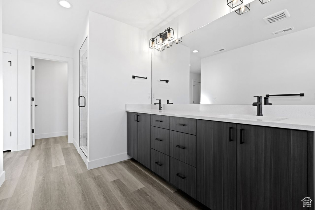 Bathroom featuring a shower with shower door, dual vanity, and hardwood / wood-style floors