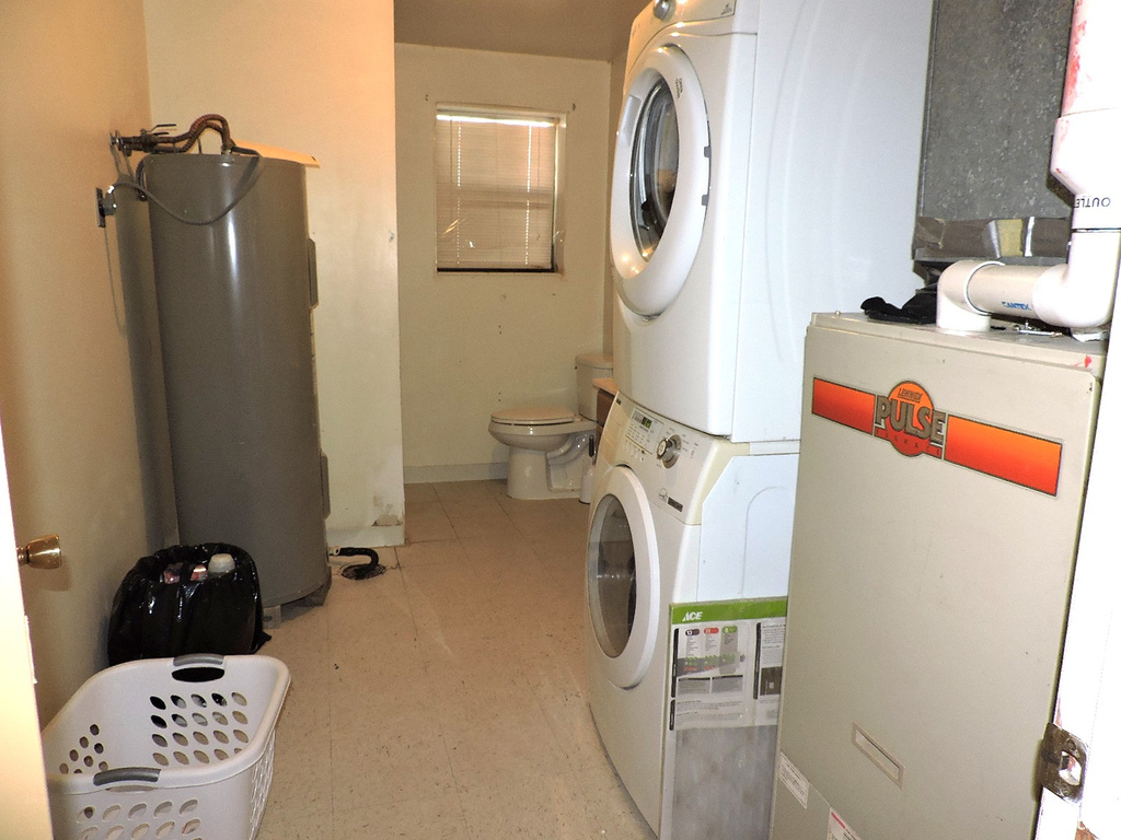 Clothes washing area featuring water heater, light tile flooring, and stacked washing maching and dryer