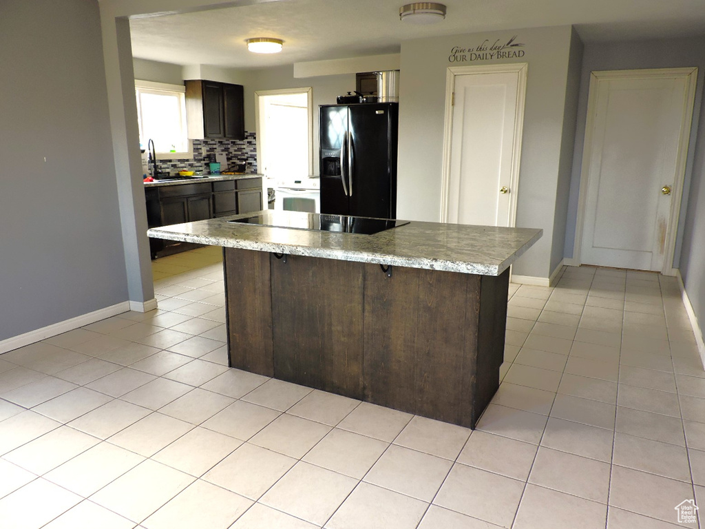 Kitchen with dark brown cabinets, light tile floors, black appliances, and backsplash