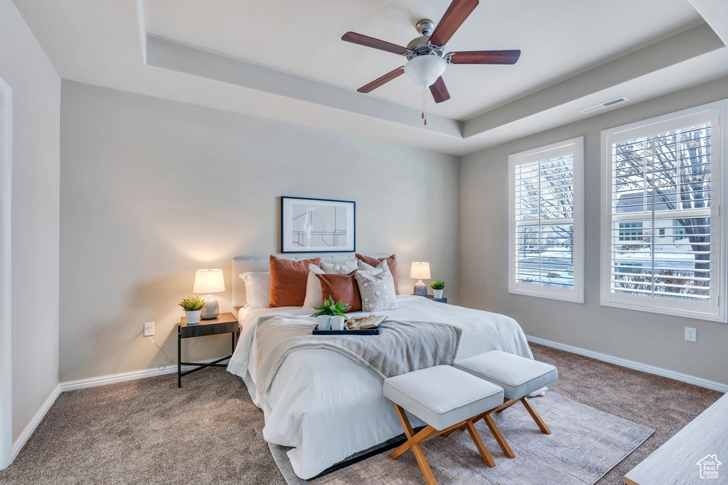 Bedroom with light colored carpet, a raised ceiling, and ceiling fan