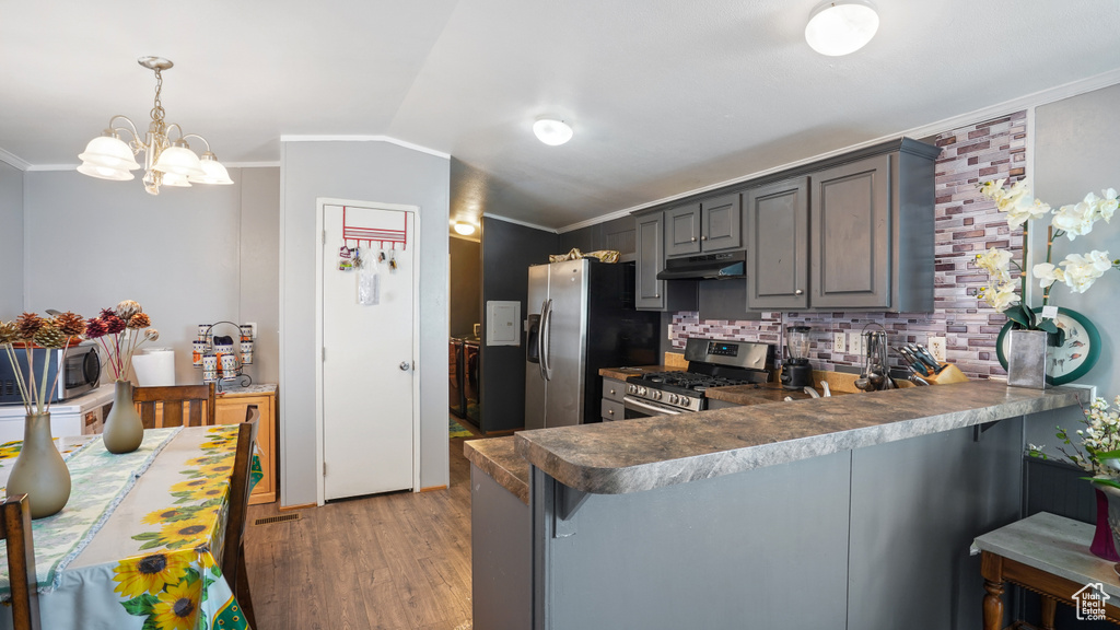 Kitchen featuring kitchen peninsula, a kitchen breakfast bar, decorative light fixtures, stainless steel appliances, and dark wood-type flooring