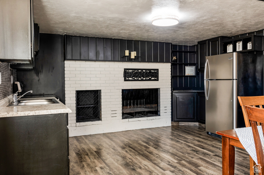 Kitchen with a fireplace, a textured ceiling, stainless steel fridge, sink, and dark wood-type flooring