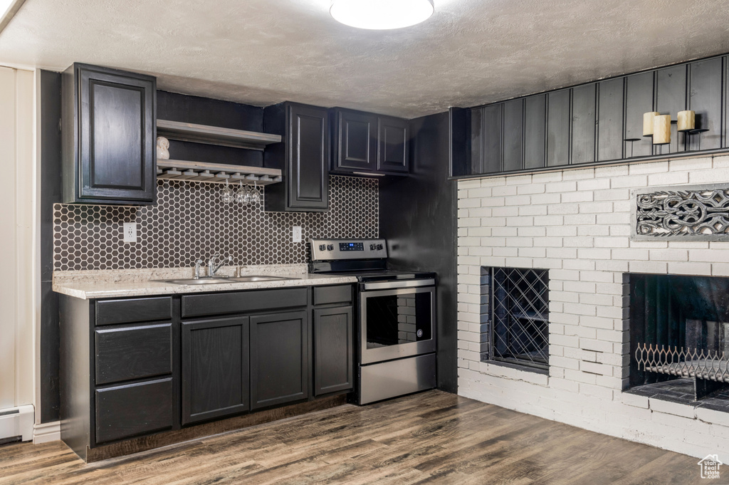 Kitchen with wood-type flooring, electric stove, sink, a fireplace, and a textured ceiling