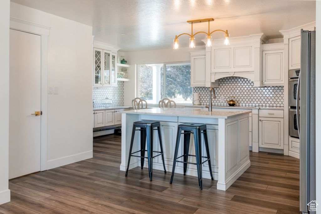 Kitchen featuring dark hardwood / wood-style flooring, decorative light fixtures, a center island with sink, and backsplash
