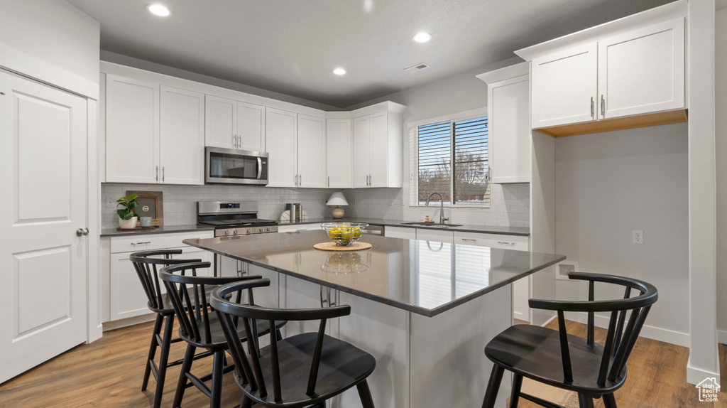 Kitchen featuring light hardwood / wood-style floors, a kitchen island, a kitchen breakfast bar, sink, and appliances with stainless steel finishes