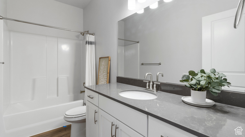 Full bathroom featuring hardwood / wood-style flooring, shower / bathtub combination with curtain, oversized vanity, and toilet