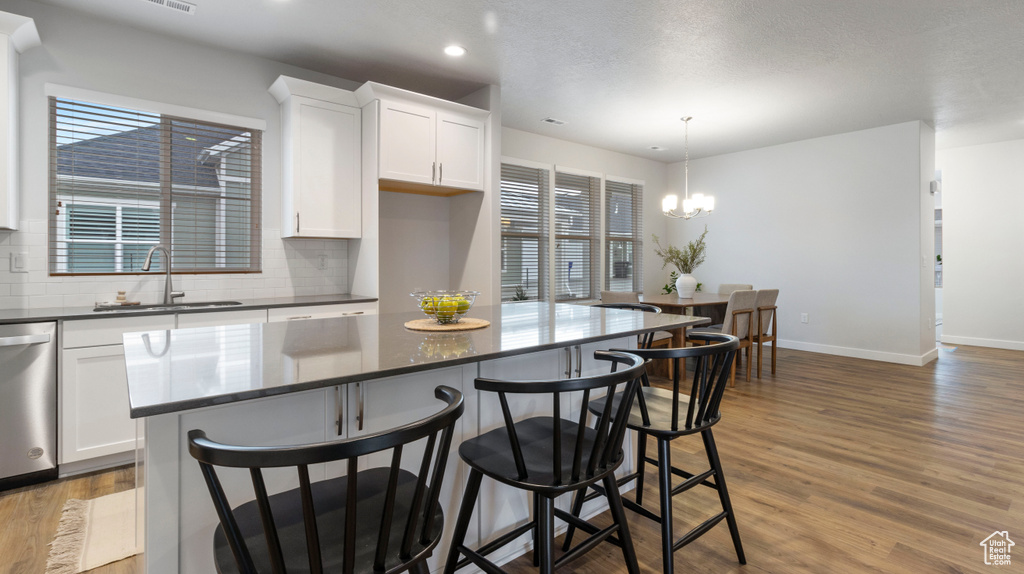 Kitchen with tasteful backsplash, white cabinetry, light hardwood / wood-style floors, and a chandelier