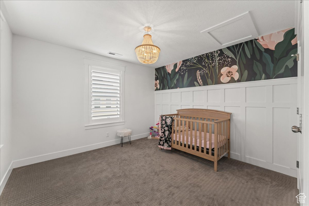 Bedroom with a nursery area, dark colored carpet, and a notable chandelier