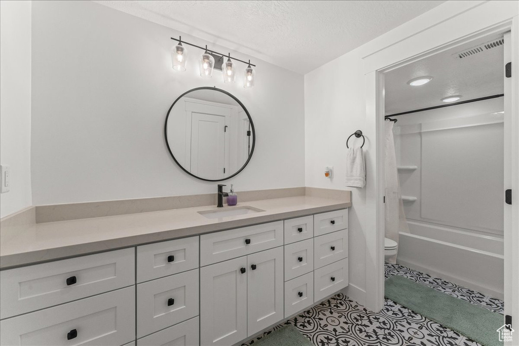 Full bathroom featuring toilet, vanity, shower / bath combo with shower curtain, tile flooring, and a textured ceiling
