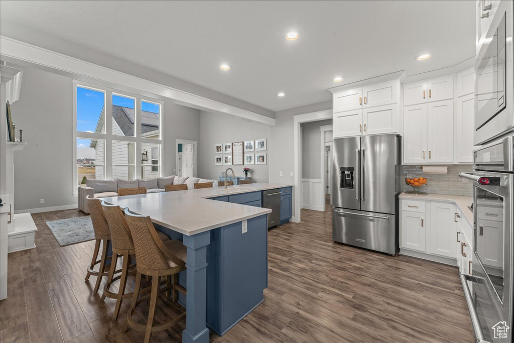 Kitchen featuring a breakfast bar area, appliances with stainless steel finishes, backsplash, dark hardwood / wood-style floors, and white cabinets