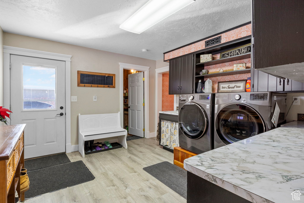 Laundry room featuring independent washer and dryer, cabinets, light hardwood / wood-style floors, and a textured ceiling