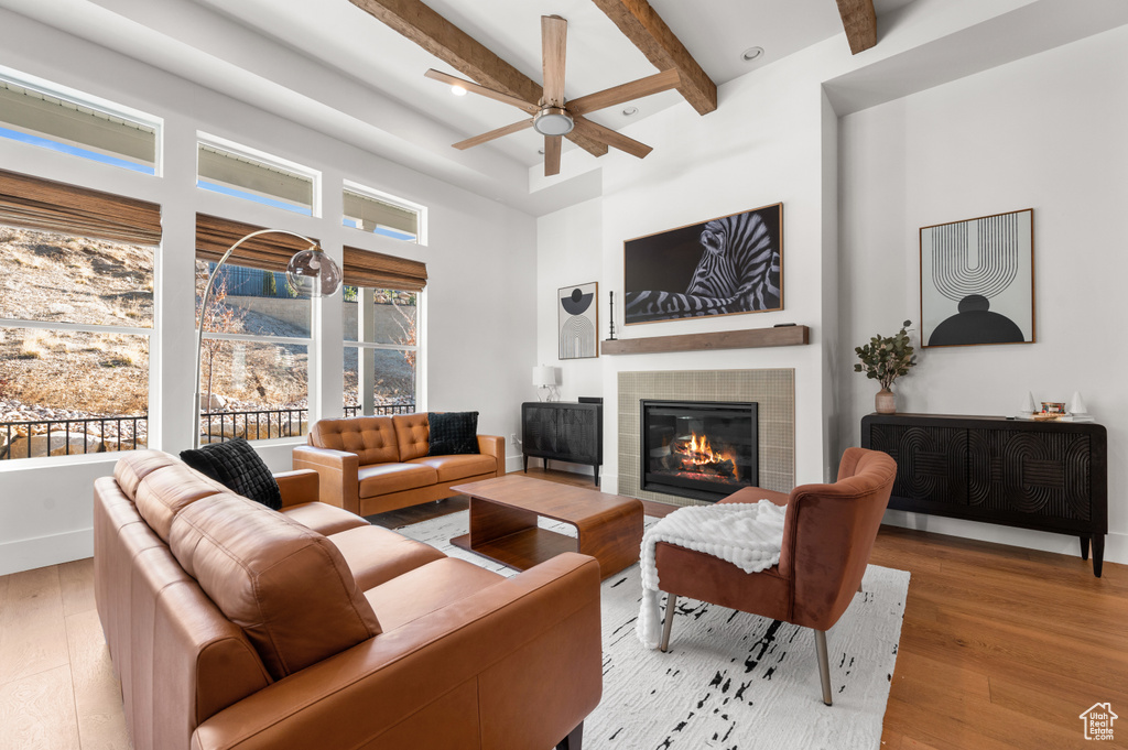 Living room with a towering ceiling, ceiling fan, beam ceiling, light hardwood / wood-style flooring, and a fireplace