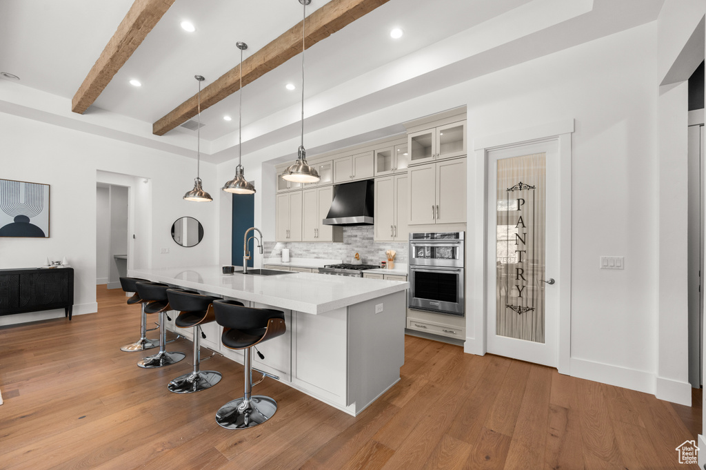 Kitchen featuring a breakfast bar, a kitchen island with sink, decorative light fixtures, light hardwood / wood-style flooring, and wall chimney range hood